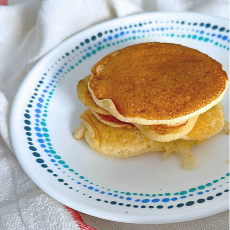 a stack of five lightly golden fluffy and delicious looking pancakes on a white plate